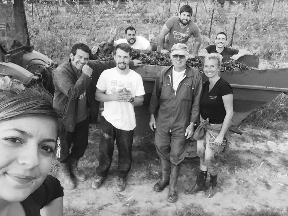 Selfie de groupe en noir et blanc de l'equipe de vendangeurs dans les vignes, devant une remorque pleine de raisin, tout le monde sourit. Photo d'equipe authentique et conviviale, parfaite pour creer la confiance.