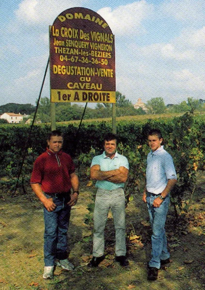 Portrait des trois vignerons de la famille Senquery debout devant les vignes, bras croisés, avec le panneau du domaine en arriere-plan. Photo authentique et tres valorisante (l'humain au coeur de l'exploitation familiale). Resolution limitee mais sujet rare et fort.