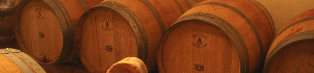 Banniere panoramique de barriques de chene empilees dans le chai, tons chauds, marque 'Boutes Tonnellerie de France' sur les fonds. Belle ambiance de chai.