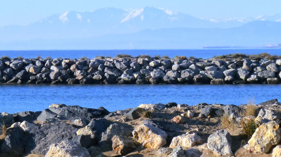Vue 'mer et montagne' depuis le terroir de Vendres Plage : enrochements, etang, la mer Mediterranee et les Pyrenees enneigees (Canigou) en fond. Paysage lumineux qui situe le domaine entre mer et montagne.